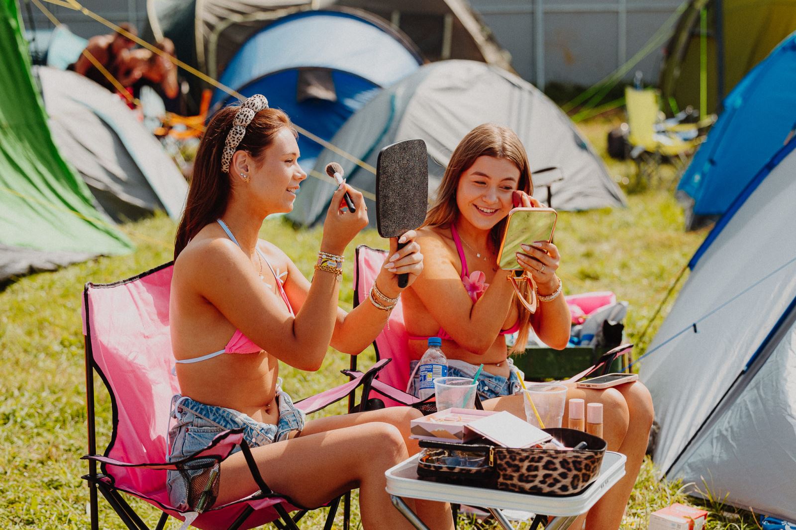 Two girls putting on makeup outside their tents
